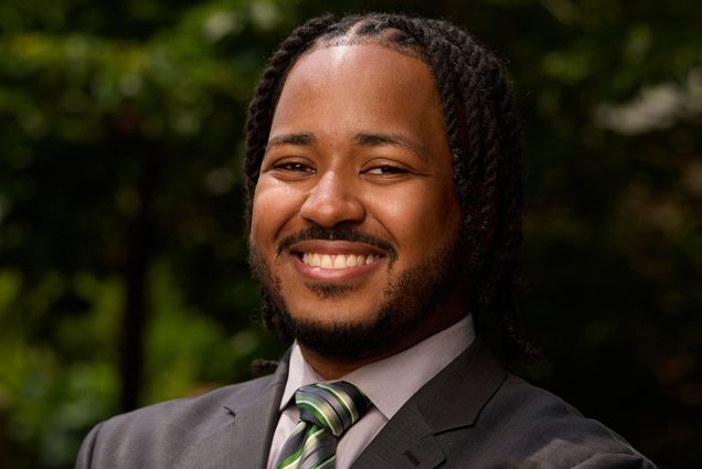Photo: Stephen Ellis of BU Campus Planning & Operations smiling in a suit in front of greenery