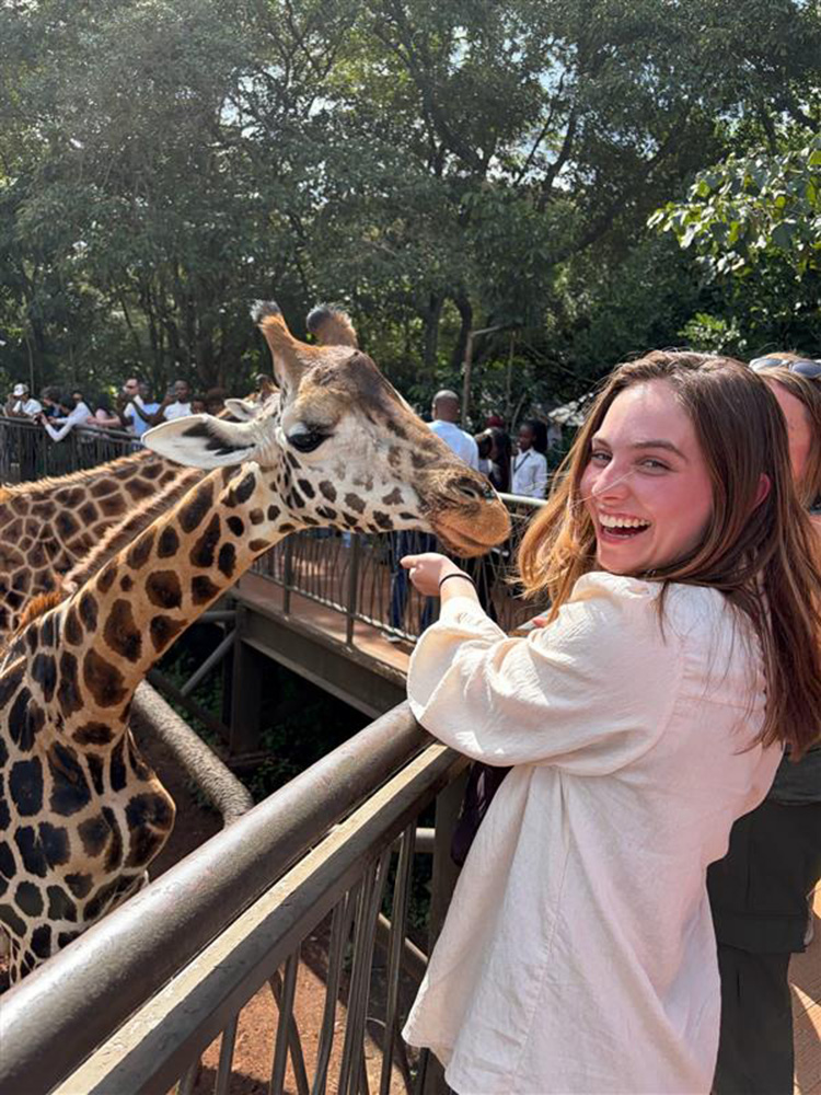 Photo: College student smiles while petting a giraffe