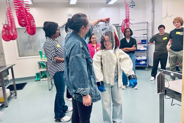 Photo: The 2026 cohort of Summer Institute in Biostatistics and Data Science (SIBS) visit BU’s National Emerging Infectious Diseases Laboratories and try on a part of a suit