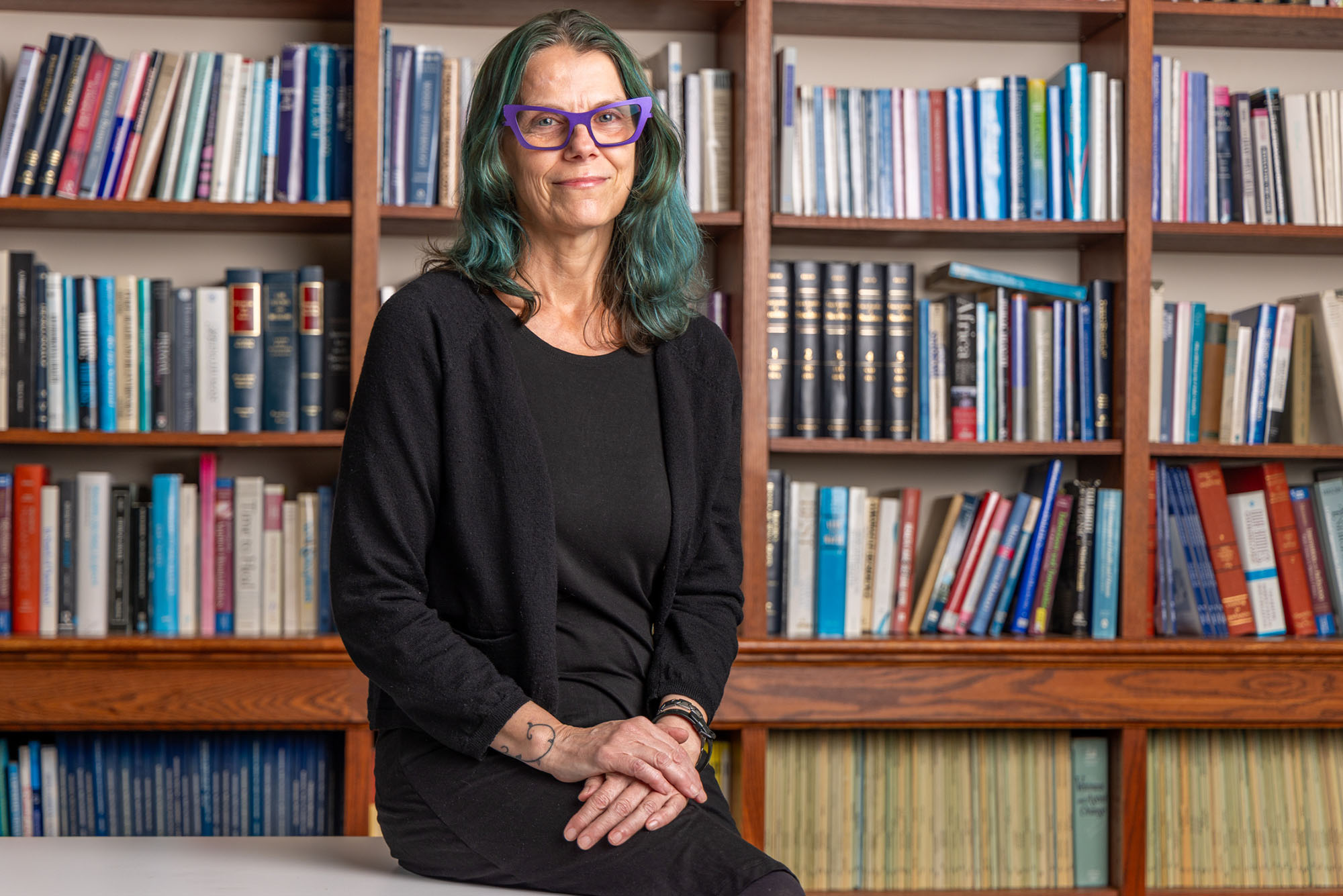 Photo: Jen Beard poses for a formal portrait in front of a large wall of books