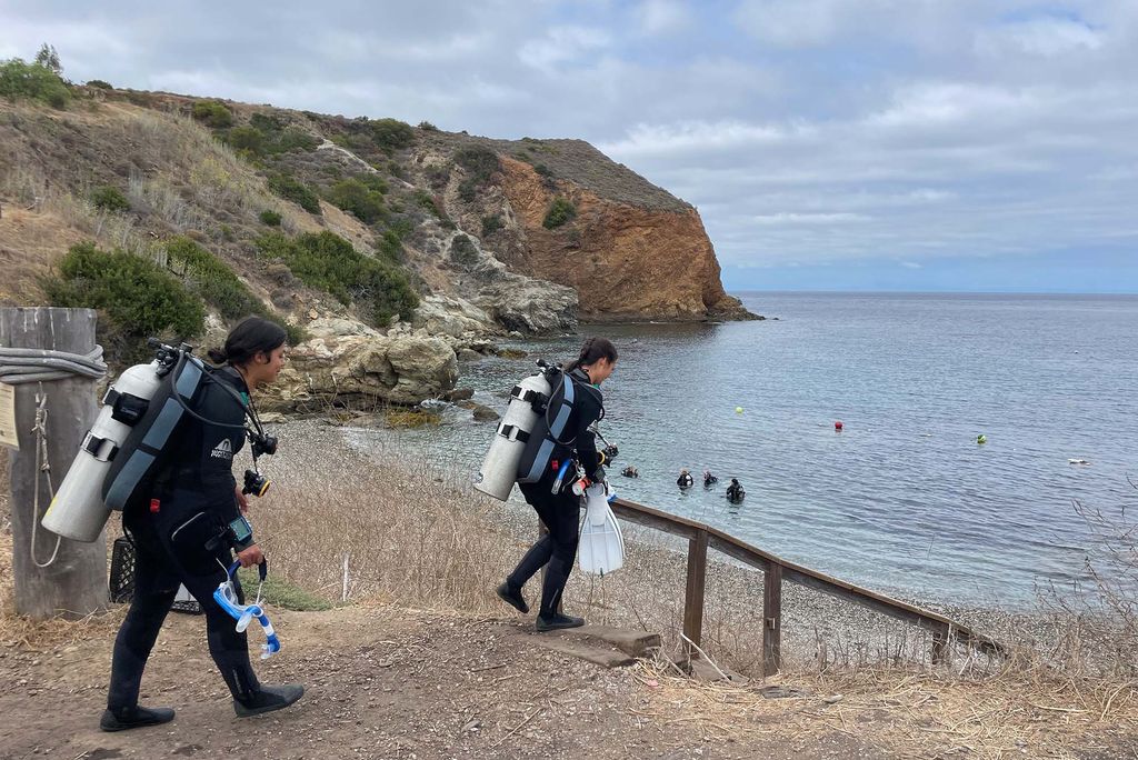 Sarah Salinas (CAS’28) (left) and Marielle Legaspi (CAS’27) head toward the water for a scuba dive at Camp Emerald Bay. Students earned multiple diving credentials during the program, including Open Water, Advanced Open Water, and Rescue Diver certifications.