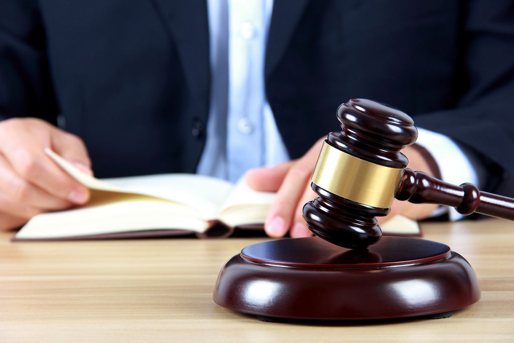 Photo: A wooden judge’s gavel rests on its sound block in front of a person reading an open book.