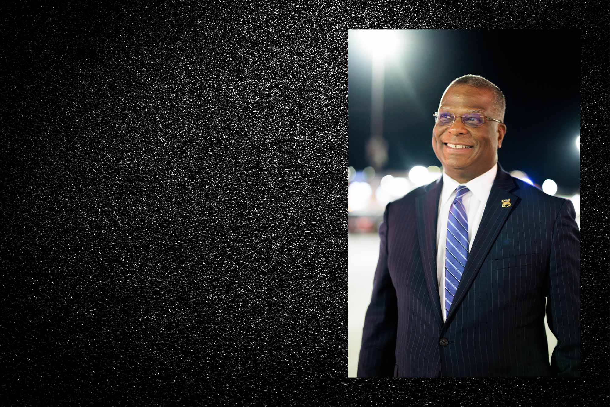 Image: Black background with many tiny white dots that imply a starry night sky. A photo of Boston Commissioner Michael Cox is shown on the right. Photo: Boston police commissioner Michael. A Black man wearing glasses, a navy blye suit and blue striped tie, smiles as he looks to the distant left. the right side of his blazer has a gold pin and he stands in front of a blurry city background.