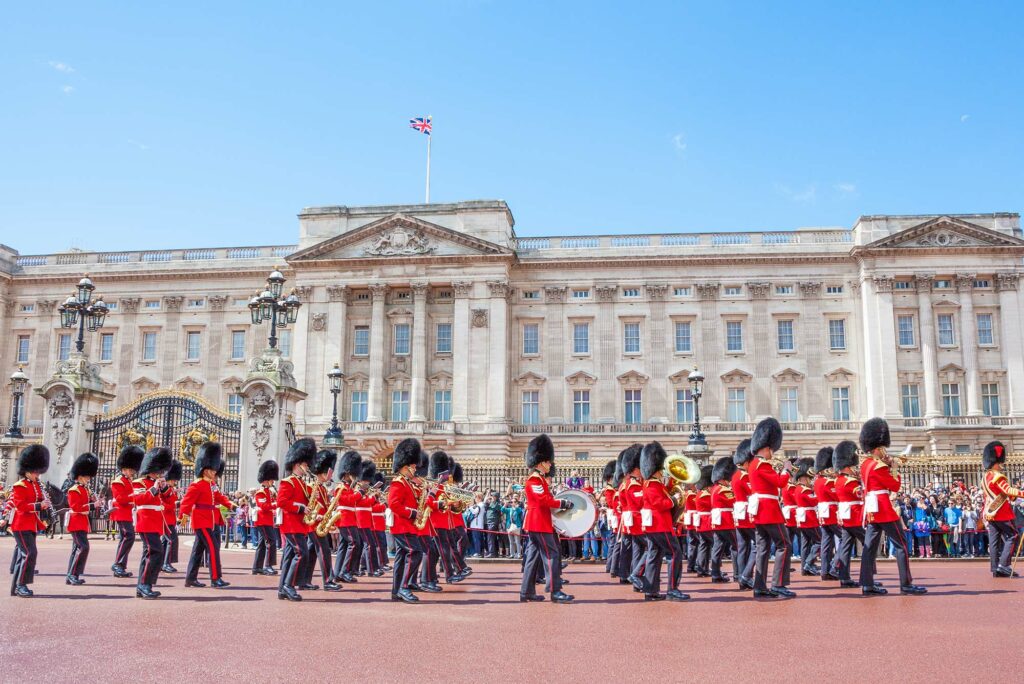 Photo: The entire King's Guard marches in uniform in front of Buckingham Palace. They wear their red uniforms with navy pants and white and gold detailing.