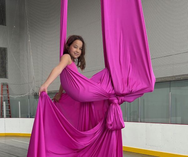 A young person sits suspended in bright pink aerial silks.