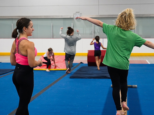 A child on a balance beam learns from an instructor at FitRec's tumbling program.