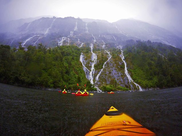 2016 GP Photo Contest 3rd place winner kayaks on a river in the rain facing a mountain with waterfalls in New Zealand