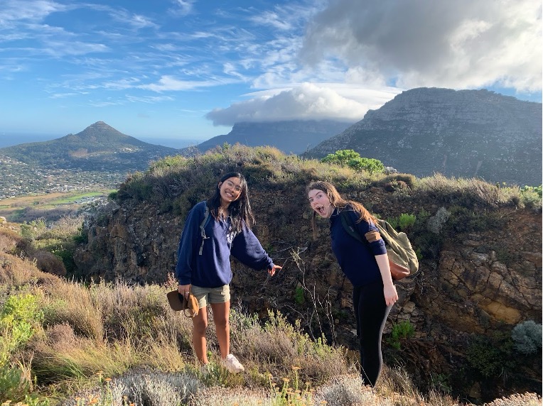 Violet Barton and a friend hiking to an abandoned cobalt mine in Cape Town, pointing at a fissure in the ground containing cobalt.