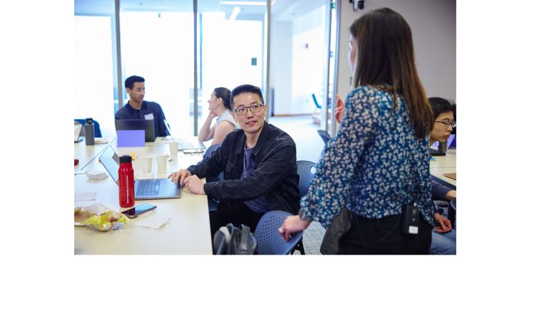A student sits at his desk, listening attentively as his professor speaks to him.
