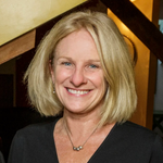 Headshot of woman with shoulder-length blonde hair, wearing a black shirt, smiling.