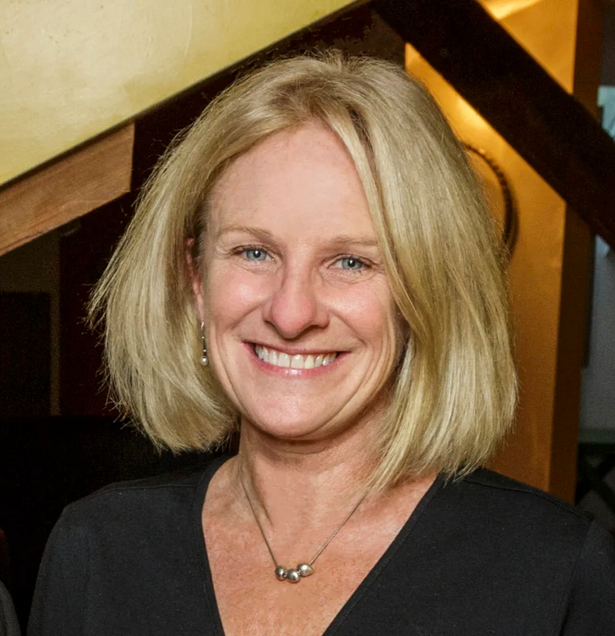 Headshot of woman with shoulder-length blonde hair, wearing a black shirt, smiling.