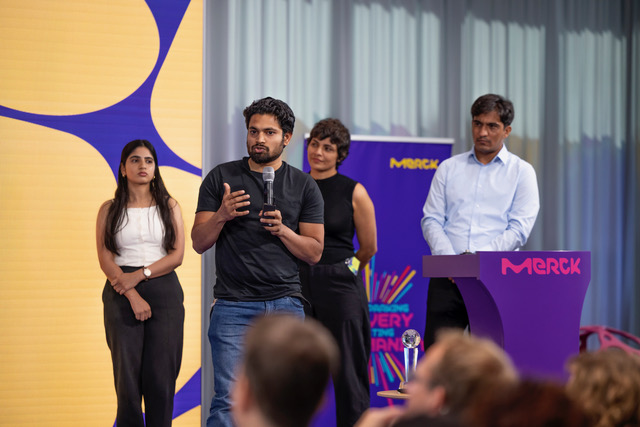 students presenting at a competition, standing on a stage, one with microphone in hand
