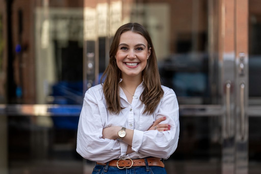 Photo: Grad student Lindsey Cohen, a young white woman wearing a white shirt, poses for a thumbnail photo for her terriers in charge video produced by the BU Today team.