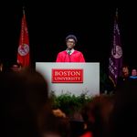 Photo: BU Student Government President Akwasi Antwi talking behind a podium that says "Boston University" while wearing a red academic gown