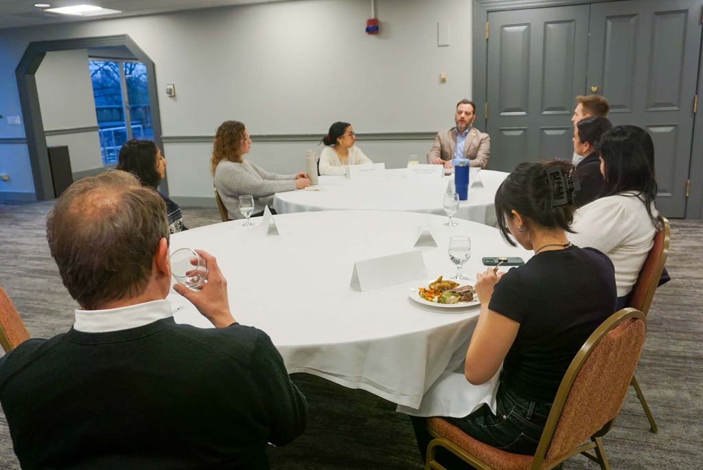 Photo: A group of individuals, mainly students, sit around two white clothed round tables.