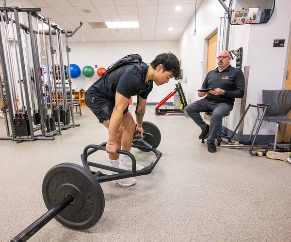 Photo: A young man with a mechanical contraption on his back to assist with his deadlifts.