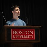 Photo: A white man with short brown hair and a dusty blue shirt on a podium.