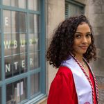 Photo: A young woman with short, curly hair poses in front of BU's Newbury Center in her graduation regalia.