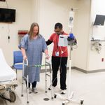 Photo: Krishn More (SAR 26) pretends to assist Corinne Fairweather, Manager of the Mobility Program during training at the Sims lab