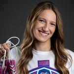 Photo: Hannah Bryson, a female wrestler at BU, holding up purple wrestling shoes and posing with a smile