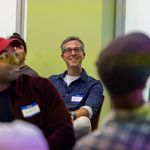 Photo: A group shot of people sititng in chairs with Eric Gordon, director of COM’s Center for Media Innovation & Social Impact, in the center