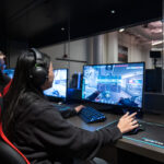 Photo: A young BU student plays an online game at Balance Patch, the on-campus video game lounge. She sits in a gaming chair, looking at a computer screen and plays with a keyboard and mouse.