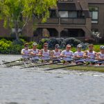 Photo: A group of men row a large boat with oars, they are all wearing matching red uniforms and tank tops