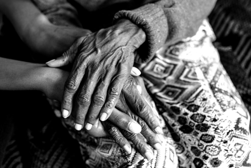 Photo: Black and white close up shot of an older, Black women's hands resting on a blanket.