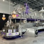Photo: A huge metal sculpture with LED lights on the bottom and wired lights on the top, hooked to a chandelier. The sculpture is in a warehouse with a black curtain in the back and exposed pipping on the ceiling.