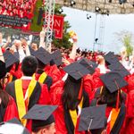 Boston University students in their caps and gowns, looking up at the stage at Commencement on Nickerson Field.