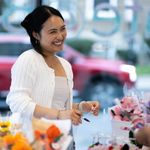 Photo: A woman manning a arts table market smiles as she talks to a customer.