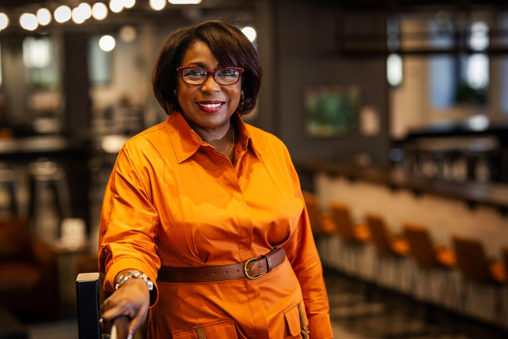 Photo: Michele Courton Brown (CAS’83), a Black woman with short hair, red glasses, wearing a persimmon color dress, smiles for the camera. Brown is the chair of YouthBuild USA board of directors poses for a photo on May 22, 2024. She’s the first woman and the first Black woman to lead the body.