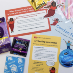 This is a photo from Boston University's Student Health Services, showcasing aspects of from their condom fairy program. There are pamphlets, fairy stickers, and different types of condoms, all spread out on a table.