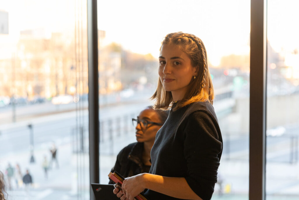 Photo: Vicky Plasencia looks into the camera and gives a small smile. Behind her is a large window looking out onto BU's campus.