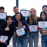 Photo: Group photo of various students standing in front of a large window and smiling and holding up certificates that read "Grandlabbies".