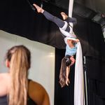 Photo: A woman in athletic clothing is wrapped up in a hanging fabric, performing aerial acrobatics.