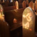 Photo: A picture of open pews with the sun reflecting the light in an empty church.