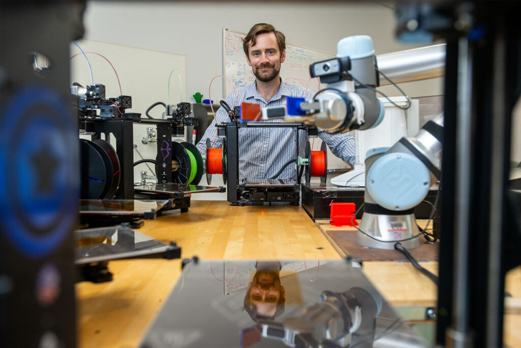 Photo: Keith Brown, an ENG associate professor of mechanical engineering, stands with autonomous researching robot, MAMA BEAR, in his lab at BU. Structures like these inform the robot’s search for efficiency, and contribute to the larger mission of autonomous research.