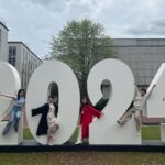 Photo: A group of graduating college students in robes and mortarboards celebrate under a large group of numbers reading "2024" in an urban display in Boston