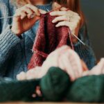Photo: A young woman knitting with balls of yarn on the table in front of her, in various colors