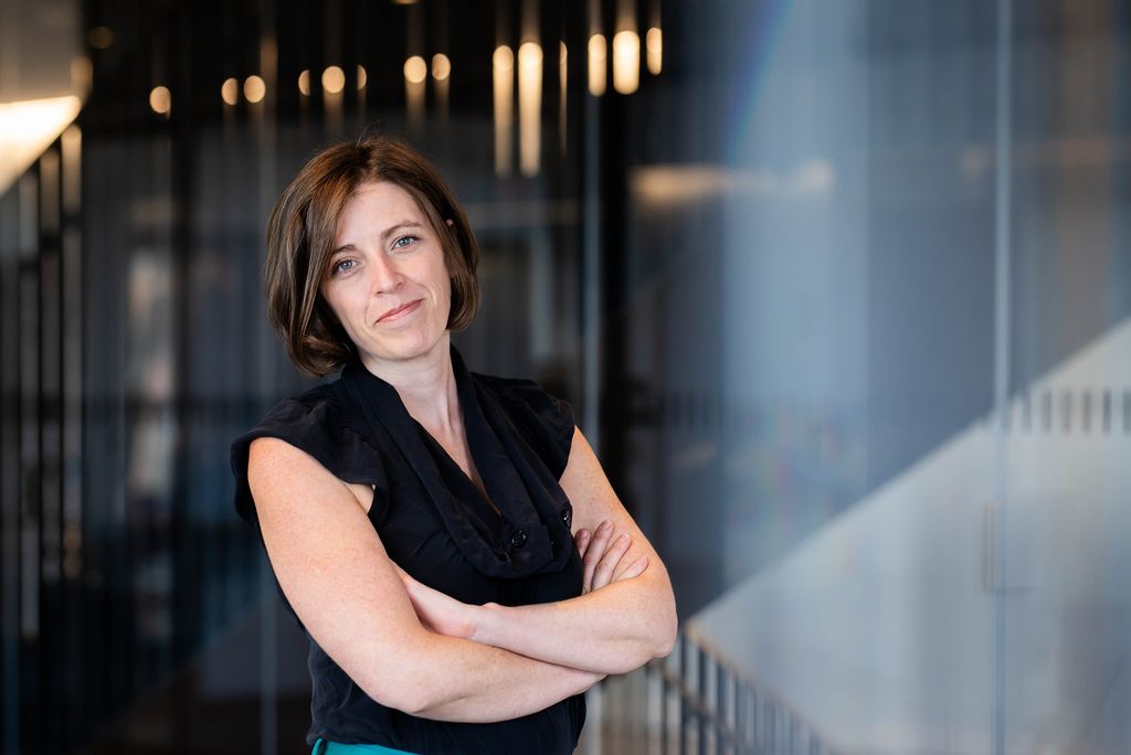 Photo: A woman with short hair leans against a blue wall in this posed formal portrait