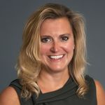 Photo: A white woman with blonde hair in front of a gray background smiles for portrait photo.