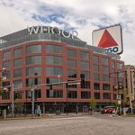 Photo of the multi-use building that is also the WHOOP headquarters in Kenmore Square. The building is brick with large blueish windows. A large grey "WHOOP" sign is prominent atop. A large CITGO sign can be seen peeking from behind the building.