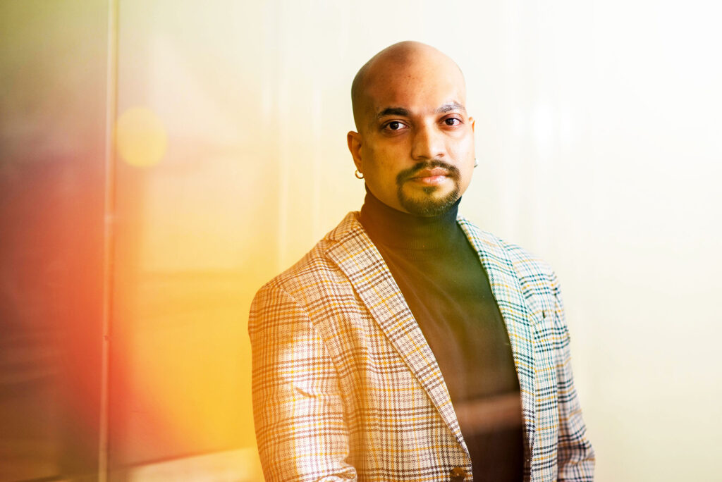 Photo: A picture of a man looking at the camera. He has on a patterned blazer and turtleneck sweater