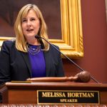 Photo: Melissa Hortman wearing a blazer and standing behind a podium that says "Melissa Hortman, Speaker"