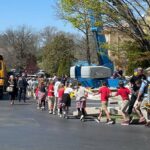 Photo: A line of children hold hands as they are ushered out of their school after a school-shooter threat. They were variations of their school uniform and are walking towards a school bus.