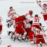 Photo: A dogpile of the BU hockey team after a big win. They are on the ice with their white uniforms and red detailing.