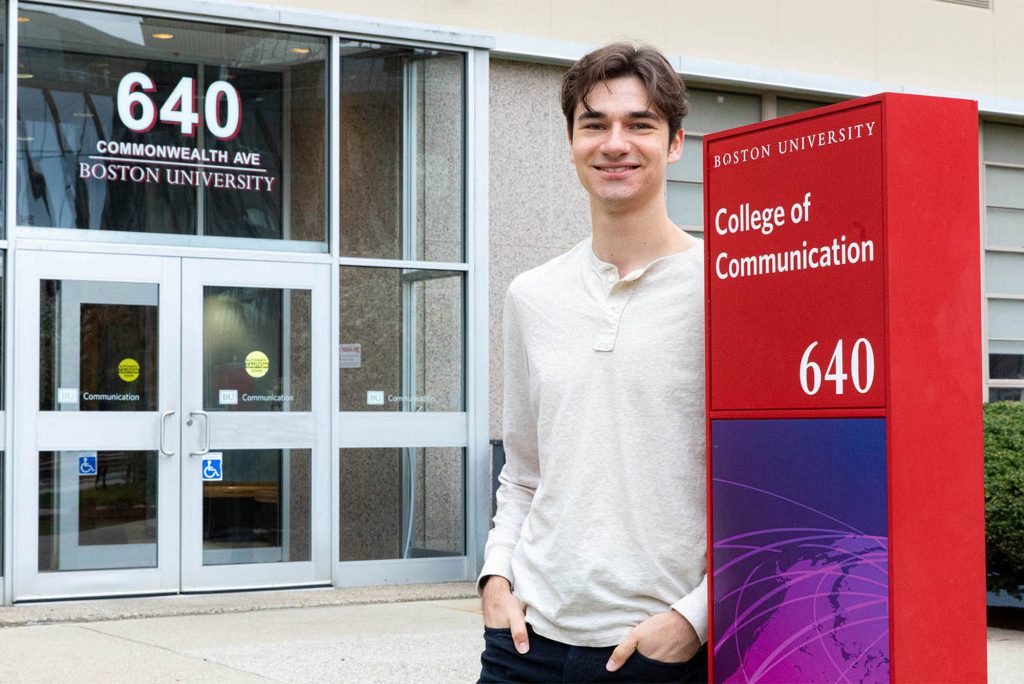 Photo: Will Loggia, a tall white college student wearing a long sleeve shirt stands in front of 640 Commonwealth Ave in Boston, the BU College of Communication.