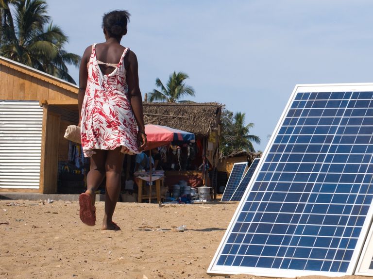 Person walking through village next to solar panels.