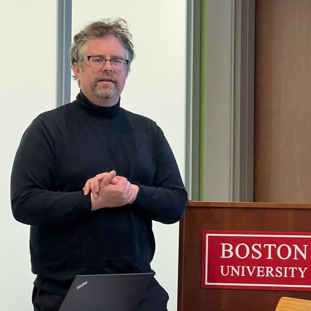 A person lectures from beside a Boston University lectern